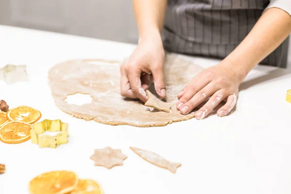 Young pretty woman prepares the dough and bakes gingerbread and cookies in the kitchen. She makes a star shape on the dough. Merry Christmas and Happy New Year. — Stock Photo, Image