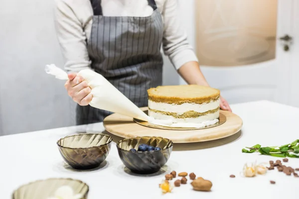 Suikerbakker met banketzak die room op taart perst in de keuken. Het concept van zelfgemaakt gebak, het bakken van taarten. — Stockfoto