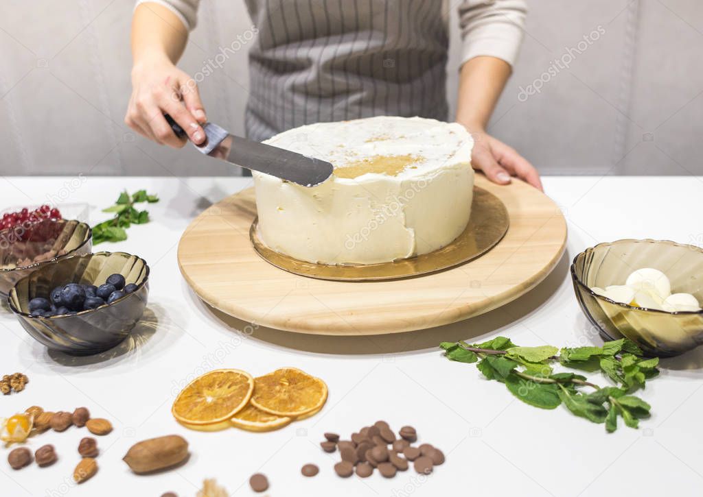 Confectioner smooths white cream on a biscuit cake with a cooking spatula. The concept of homemade pastry, cooking cakes.