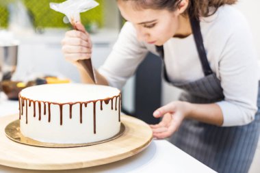 Bir şekerlemeler ahşap bir stand üzerinde beyaz krem bisküvi kek üzerine bir pasta torbası sıvı çikolata sıkır. Ev yapımı pasta kavramı, yemek pastaları.