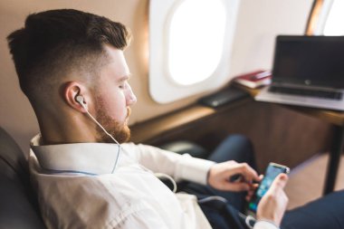 Genç ve başarılı iş adamı dinleniyor ve özel iş uçağının koltuğunda oturmuş müzik dinliyor.