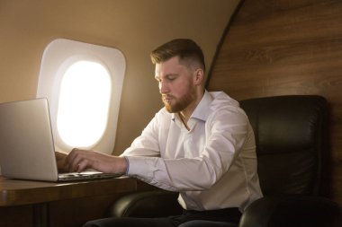 Çekici ve başarılı bir iş adamı, özel iş uçağının koltuğunda otururken çalışıyor.