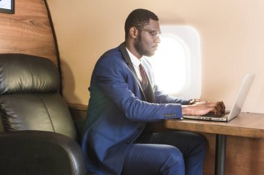 Onun özel jet sandalyede otururken gözlük bir dizüstü bilgisayar üzerinde çalışan çekici ve başarılı Afrikalı Amerikan işadamı.
