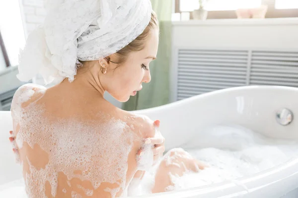 A young attractive girl relaxes in the bathroom and rests against the backdrop of a beautiful light interior. Spa treatments for beauty and health with skin care — Stock Photo, Image