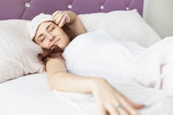 Une jolie jeune femme brune dort dans son lit avec un masque de sommeil — Photo