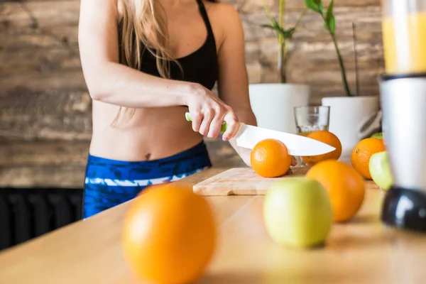 有魅力的女运动员在训练、切水果和做新鲜果汁之前，在厨房准备一份健康的早餐。健康的生活方式、健康和美丽 — 图库照片