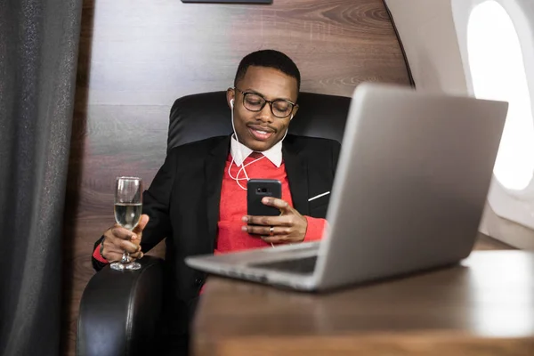 Atrakcyjny i udany African American biznesmen z okularami pracujących na laptopie siedząc na krześle jego prywatnego odrzutowca — Zdjęcie stockowe