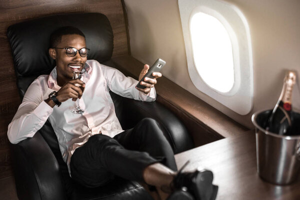 Successful young Afro American black businessman sitting in the chair of his private jet