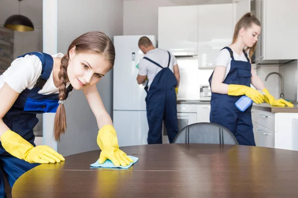 Service de nettoyage avec équipement professionnel pendant le travail. nettoyage professionnel de la kitchenette, nettoyage à sec du canapé, lavage des fenêtres et des sols. hommes et femmes en uniforme, salopettes et gants en caoutchouc — Photo