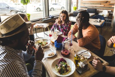 Bir kafede pizza yiyen, kokteyl içen, eğlenen çok kültürlü gençlerden oluşan bir şirket.