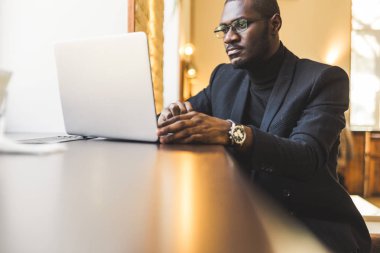 Bir fincan çay ile bir dizüstü bilgisayar arkasında çalışan bir kafede genç yakışıklı koyu tenli işadamı.