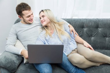 Genç güzel çift kanepede istirahat ve oturma odasında bir laptop online video izlerken.