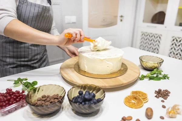 De banketbakker maakt witte room glad op een biscuittaart met een kookspatel. Het concept van zelfgemaakt gebak, het bakken van taarten. — Stockfoto