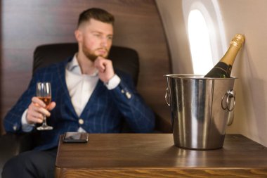 Pahalı bir takım elbiseli Genç başarılı bir işadamı elinde bir bardak şampanya ile özel bir Jet sandalyesinde oturur ve pencereden dışarı bakıyor