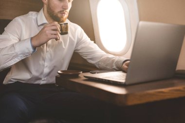 Çekici ve başarılı işadamı kahve içme ve onun özel jet bir sandalyede otururken bir laptop arkasında çalışma.
