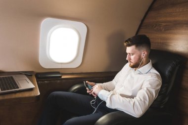 Genç ve başarılı iş adamı dinleniyor ve özel iş uçağının koltuğunda oturmuş müzik dinliyor.