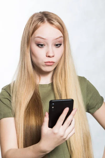 Una joven desconcertada y preocupada sosteniendo un teléfono inteligente, mirando con una expresión sorprendida . — Foto de Stock