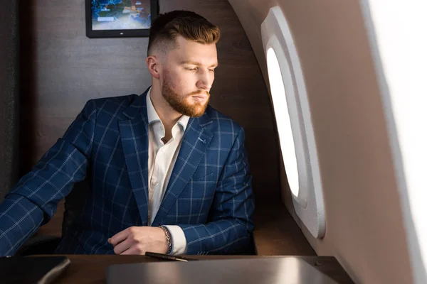 Atractivo y exitoso hombre de negocios en un traje caro trabajando sentado en la silla de su jet privado . — Foto de Stock