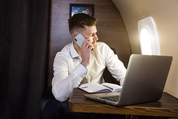 Młody, atrakcyjny i odnoszący sukcesy biznesmen rozmawiający przez telefon i pracujący na krześle swojego prywatnego samolotu biznesowego — Zdjęcie stockowe