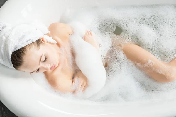 Una chica joven y atractiva se relaja en el baño y descansa sobre el telón de fondo de un hermoso interior de luz. Tratamientos de spa para la belleza y la salud con cuidado de la piel — Foto de Stock