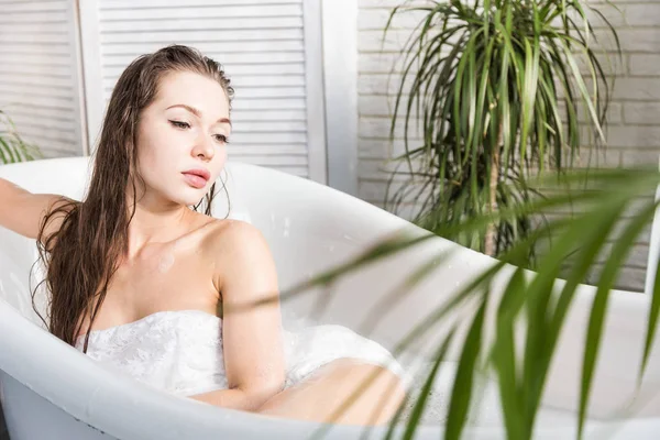 Молодая привлекательная девушка расслабляется в ванной комнате и отдыхает на фоне красивого светлого интерьера. Спа-процедуры для красоты и здоровья с уходом за кожей — стоковое фото