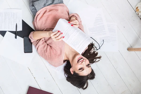Una hermosa mujer yace en el suelo entre papeles y documentos, la chica freelancer sonríe y se relaja durante un descanso del trabajo — Foto de Stock