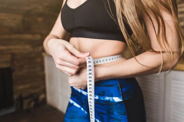 Hermosa mujer joven en ropa deportiva mide la circunferencia de la cintura de vuelo medida. Deporte, dieta y pérdida de peso —  Fotos de Stock