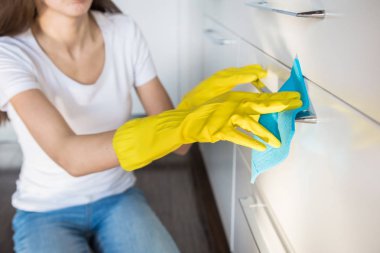 Profesyonel temizlik şirketinden genç bir kadın evi temizliyor. Bir adam mutfağı temizlik malzemeleriyle sarı eldivenlerle yıkıyor..