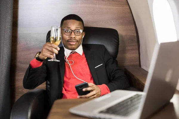 Atrakcyjny i udany African American biznesmen z okularami pracujących na laptopie siedząc na krześle jego prywatnego odrzutowca — Zdjęcie stockowe