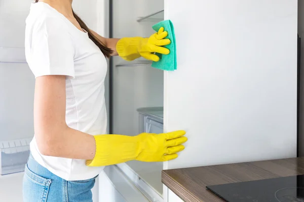 A young woman from a professional cleaning company cleans up at home. A man washes the kitchen washes the fridge in yellow gloves with cleaning supplies stuff. — Stock Photo, Image