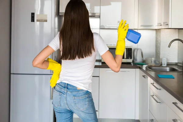 Een jonge vrouw van een professioneel schoonmaakbedrijf ruimt thuis op. Een man wast de keuken in gele handschoenen met schoonmaakspullen. — Stockfoto