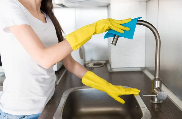 Eine junge Frau in gelben Handschuhen wäscht Kran mit einem Schwamm in der Spüle. Professioneller Reinigungsservice — Stockfoto