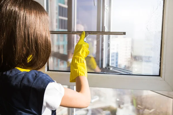 Großaufnahme einer Frau in Uniform und gelben Handschuhen, die ein Fenster mit Fensterkratzer wäscht. Professionelle Hausreinigung — Stockfoto