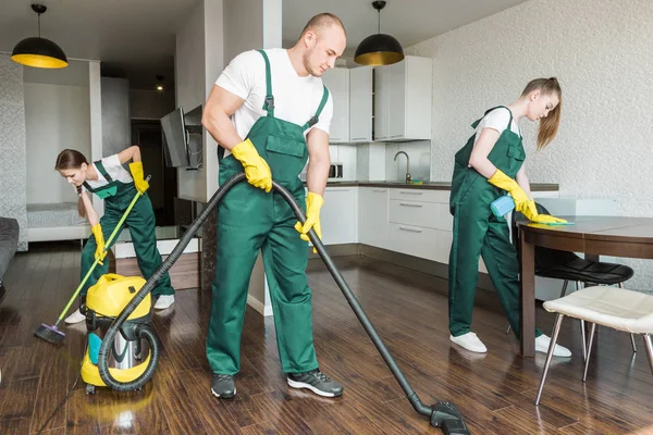 Schoonmaakservice met professionele apparatuur tijdens het werk. professionele kitchenette schoonmaak, sofa stomerij, raam en vloer wassen. mannen en vrouwen in uniform, overall en rubberen handschoenen — Stockfoto