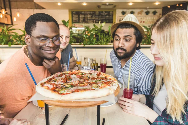 A company of multicultural  young people in a cafe eating pizza, drinking cocktails, having fun
