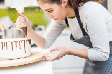 Bir şekerlemeler ahşap bir stand üzerinde beyaz krem bisküvi kek üzerine bir pasta torbası sıvı çikolata sıkır. Ev yapımı pasta kavramı, yemek pastaları.