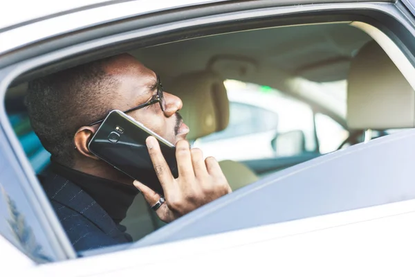 Młody biznesmen mówi na telefon siedzi na tylnym siedzeniu drogiego samochodu. Negocjacje i spotkania biznesowe. — Zdjęcie stockowe