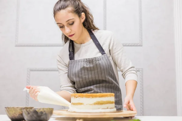 Confectioner with pastry bag squeezing cream on cake at kitchen. The concept of homemade pastry, cooking cakes.