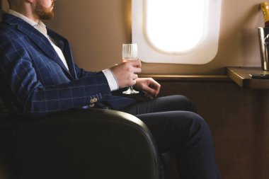 Pahalı bir takım elbiseli Genç başarılı bir işadamı elinde bir bardak şampanya ile özel bir Jet sandalyesinde oturur ve pencereden dışarı bakıyor