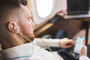 Genç ve başarılı iş adamı dinleniyor ve özel iş uçağının koltuğunda oturmuş müzik dinliyor.