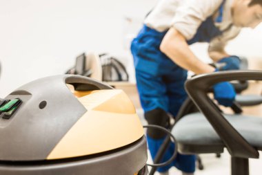 İş elbiseli ve lastik eldivenli genç adam ofis sandalyesini profesyonel ekipmanlarla temizliyor..