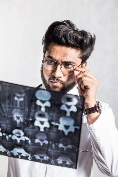 Knappe jonge arts in een witte jas met een stethoscoop controleert aandachtig de patiënten x-ray. — Stockfoto