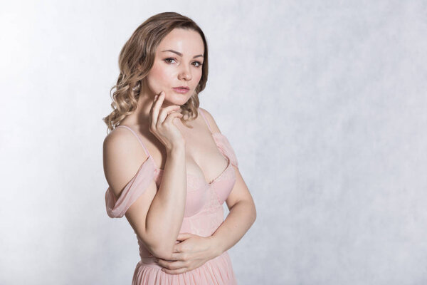 Portrait of beautiful young elegant female in pale pink wedding dress with big neckline, on a white background.