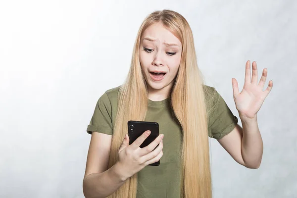 Een verbaasde en verontruste jonge vrouw met een smartphone, op zoek met een verraste uitdrukking. — Stockfoto