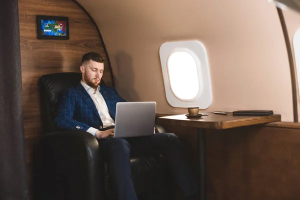 Atrakcyjny i udany biznesmen pracujący na laptopie siedząc na krześle swojego prywatnego odrzutowca. — Zdjęcie stockowe