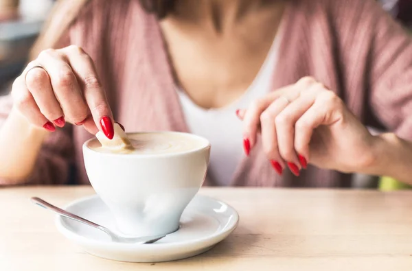 Uma menina mergulha um pedaço de açúcar no café. Close-up de mãos com unhas vermelhas make-up e copo cappuccino — Fotografia de Stock