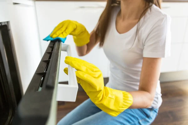 Eine junge Frau von einer professionellen Reinigungsfirma räumt zu Hause auf. Ein Mann wäscht die Küche in gelben Handschuhen mit Putzmitteln. — Stockfoto