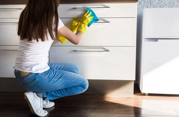 Μια νεαρή γυναίκα από μια επαγγελματική εταιρεία καθαρισμού καθαρίζει στο σπίτι. Ένας άντρας πλένει την κουζίνα με κίτρινα γάντια με καθαριστικά.. — Φωτογραφία Αρχείου