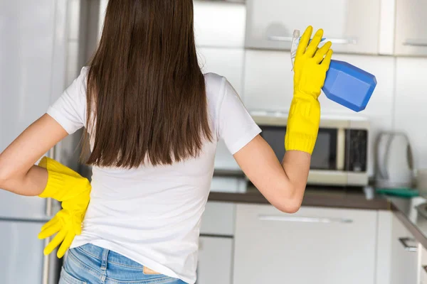 Una joven de una empresa de limpieza profesional limpia en casa. Un hombre lava la cocina con guantes amarillos con cosas de limpieza . — Foto de Stock