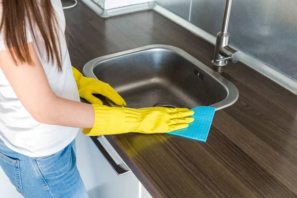 Une jeune femme en gants jaunes lave la grue avec une éponge dans l'évier. Maison service de nettoyage professionnel — Photo
